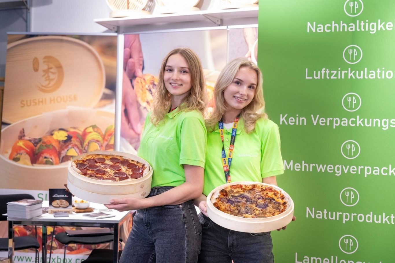 Zwei lächelnde Frauen in grünen snoxbox T-Shirts halten Pizzen in snoxboxen.